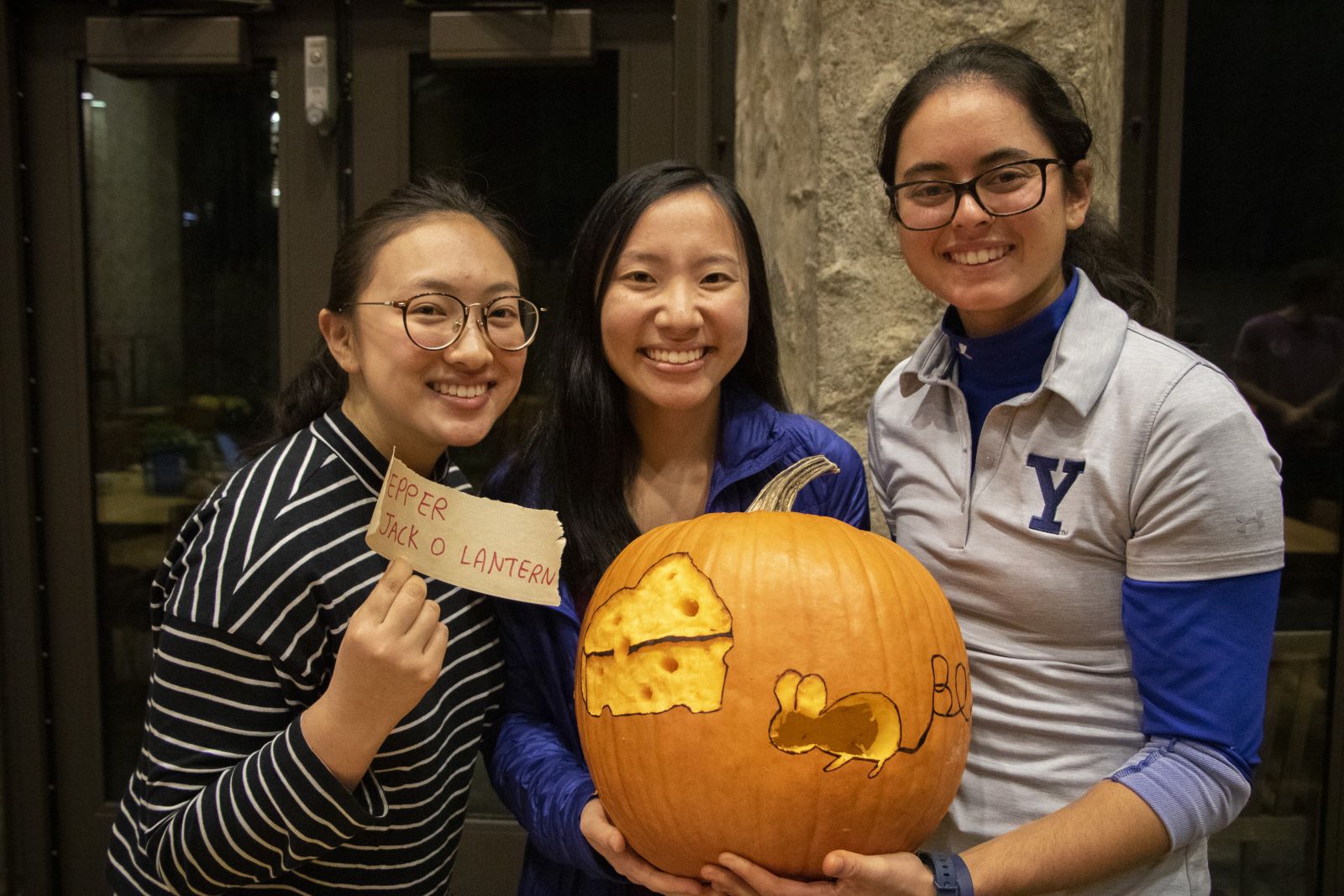 3 Yale students showing off their carved pumpkin with a design of a mouse chasing a cheese