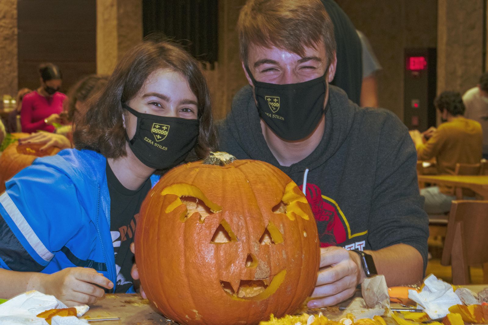 2 students with masks showcasing their big carved pumpkin