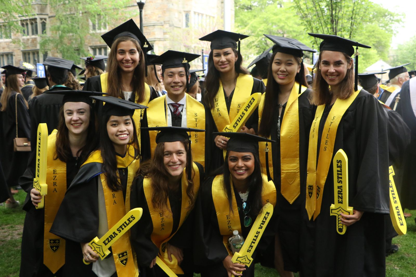 A group of graduating Stilesians holding prop yellow swords with the words "Ezra Stiles"