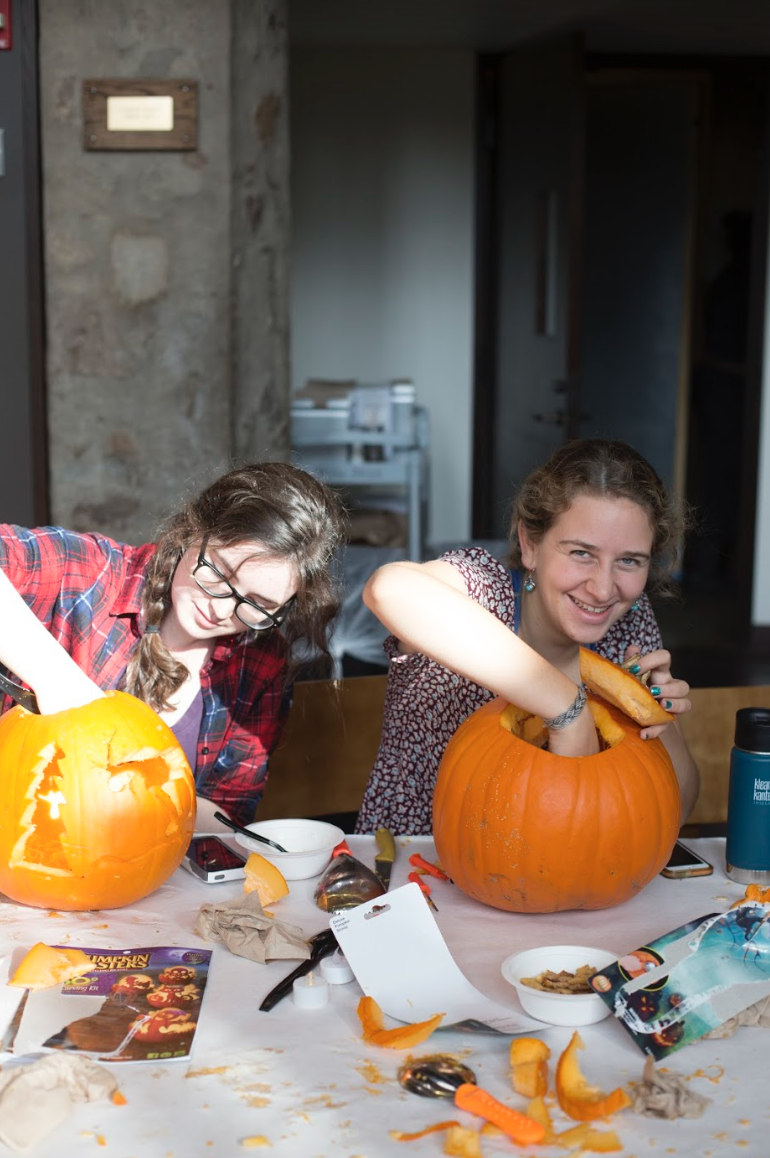 2 students taking out the pumpkin insides in their carved pumpkins