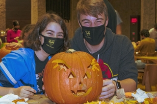 2 students with masks showcasing their big carved pumpkin